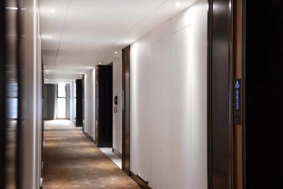 A modern hotel corridor with a wooden floor, white walls, and a series of doors leading to rooms.