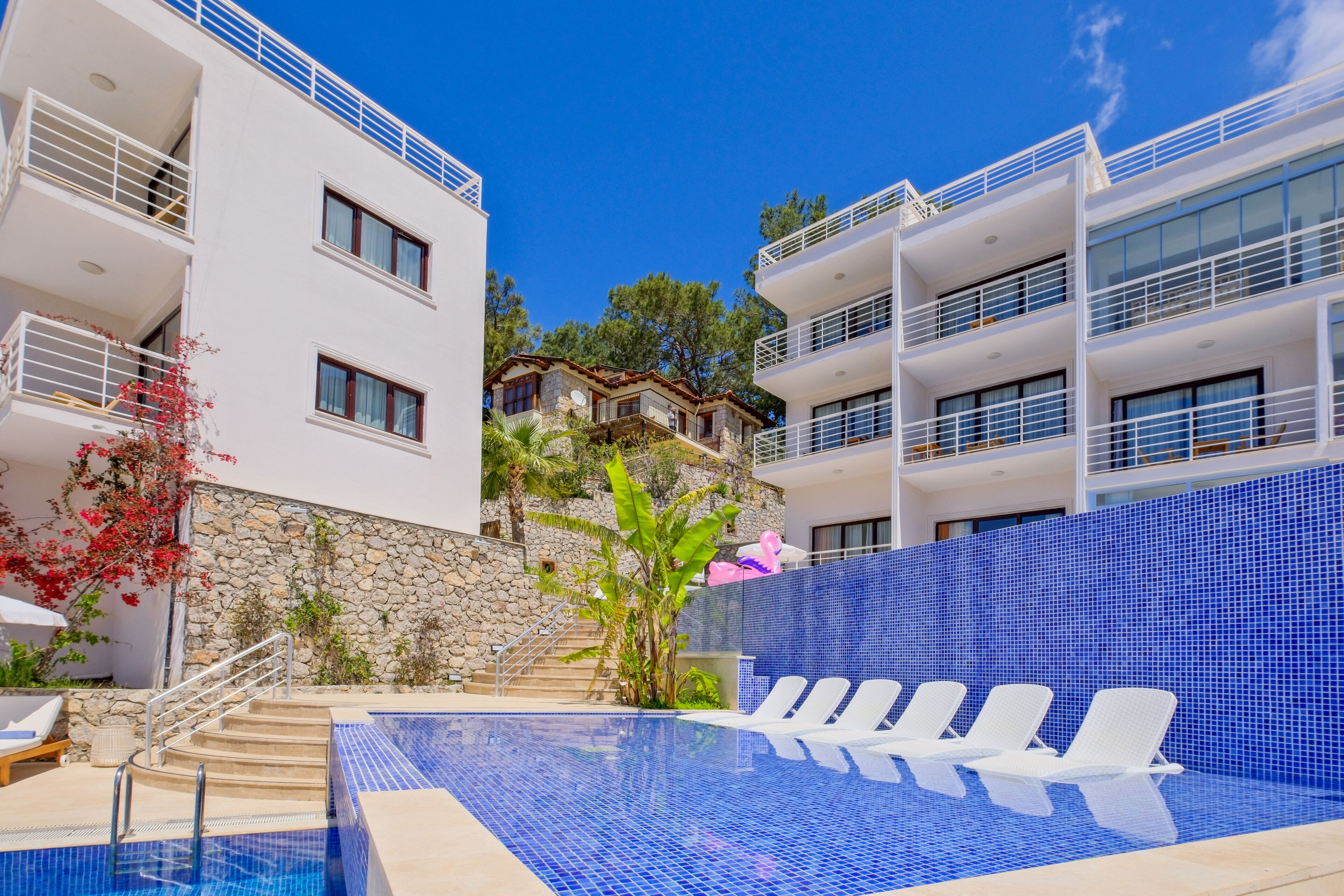 A modern hotel with a pool area, including lounge chairs and a staircase leading to a stone building.