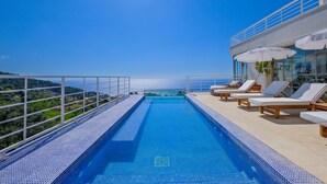 Ein Dachpool mit Infinity-Kante, Liegestühlen und einer Glasbrüstung mit Blick auf eine malerische Landschaft.
