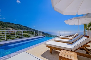 A poolside area with lounge chairs and umbrellas, overlooking a clear blue sea and a hilly landscape. - Highclere Hotel and Spa (Fethiye)
