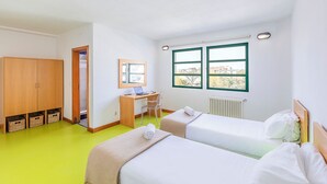 Une chambre avec deux lits, un bureau, une chaise, une armoire et une fenêtre donnant sur un beau paysage.