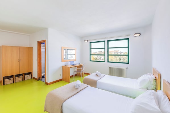 Una habitación con dos camas, un escritorio, una silla, un armario y una ventana con vistas.