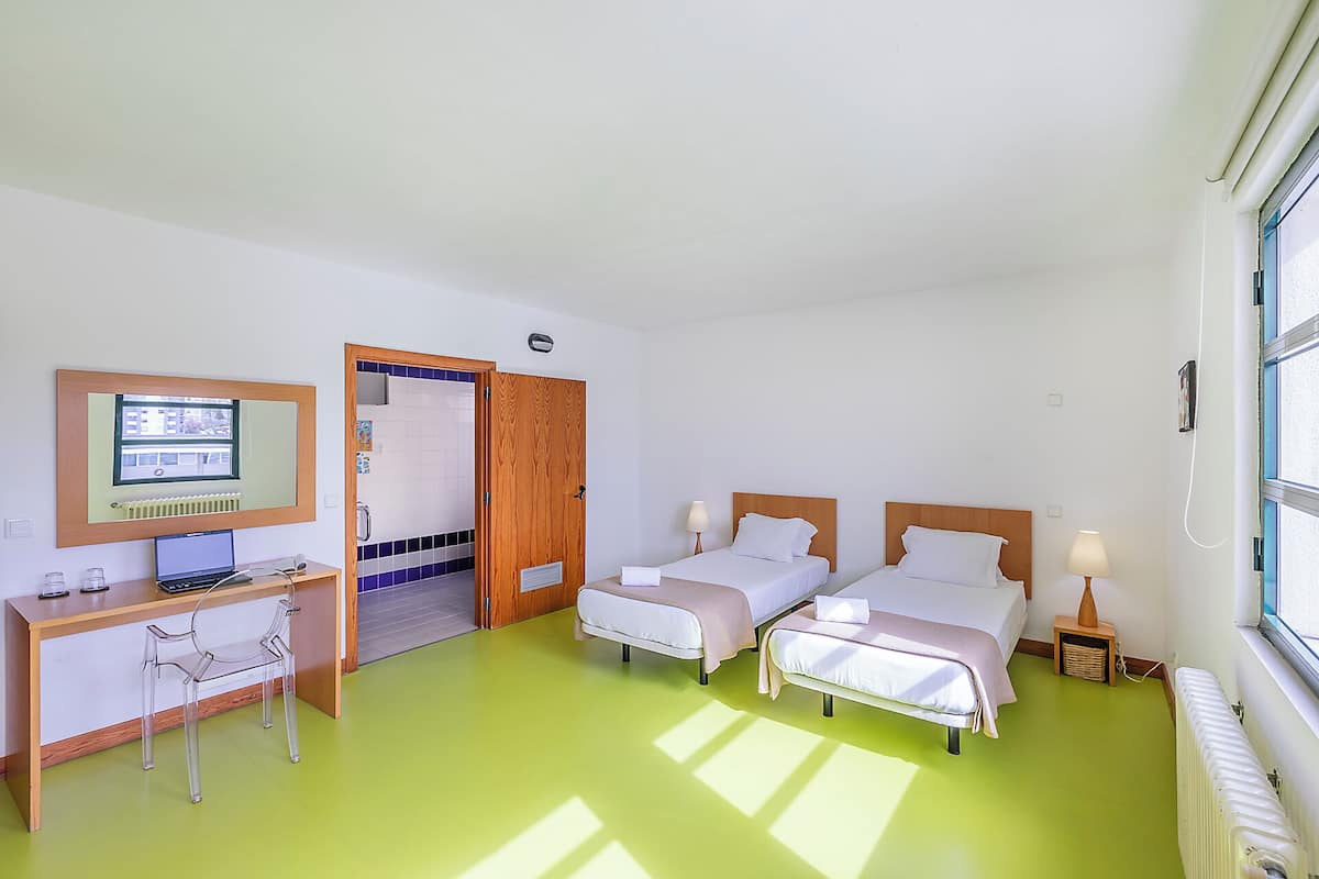 Een hotelkamer met twee bedden, een bureau met een computer, een stoel en een raam.