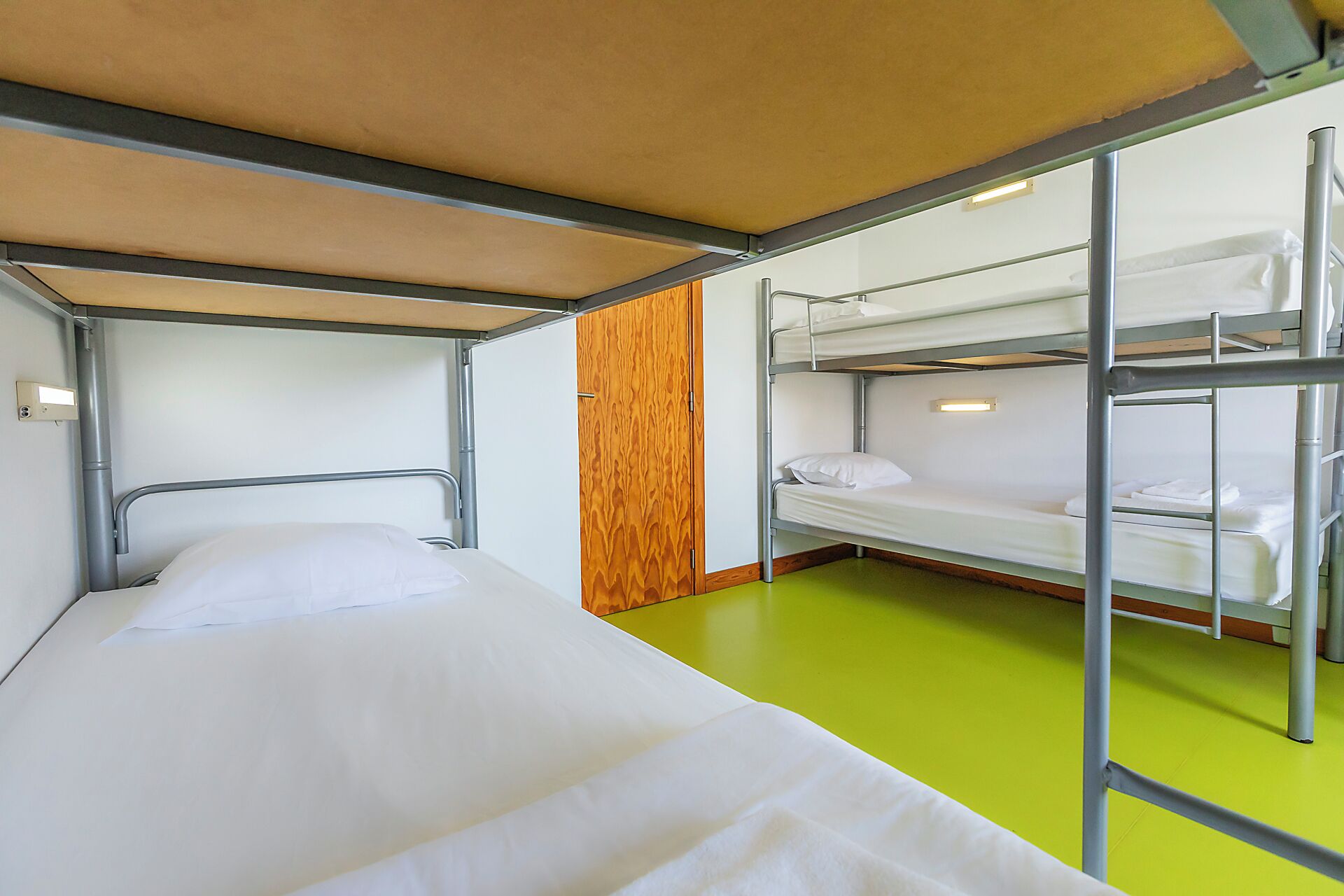 Dormitorio con literas, una cama individual y dos literas adicionales, paneles de madera en una pared y suelo verde.
