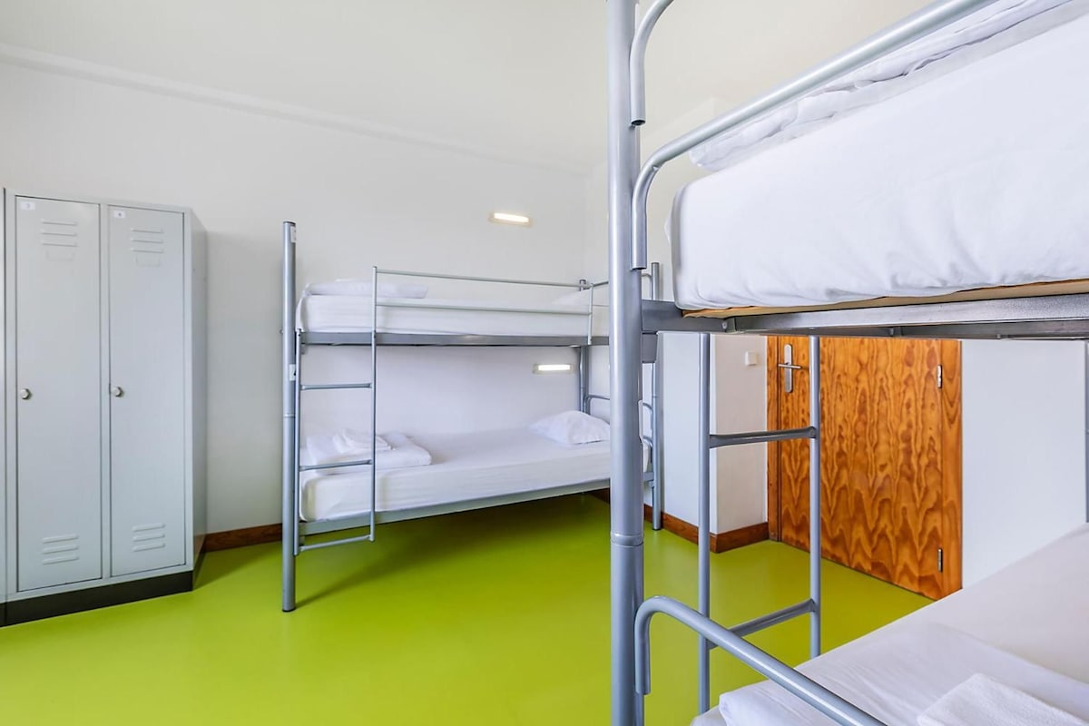 A bunk bed room with a green floor, metal bunk beds, a wardrobe, and a wooden door.