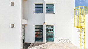 Un bâtiment à la façade blanche, une porte avec des panneaux de verre et une structure métallique jaune sur le côté droit.