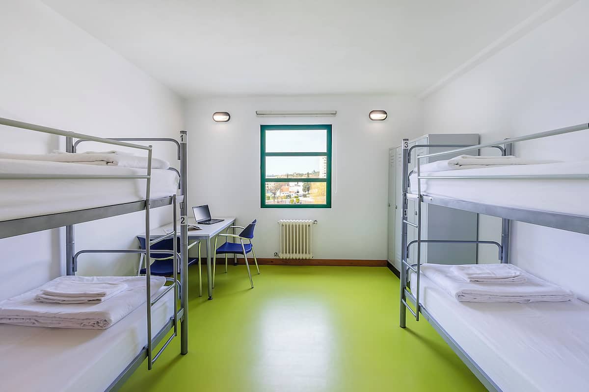 Een studentenkamer met stapelbedden, een bureau, een stoel en een raam met uitzicht.