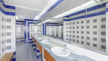 A public restroom with three sinks, a wooden bench, and blue and white tiled walls.
