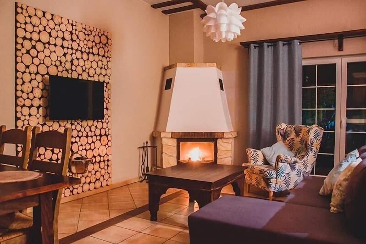 A cozy living room with a fireplace, a television mounted on a log-patterned wall, and a comfortable seating area.