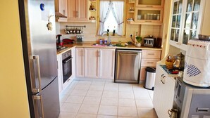 A compact kitchen with a refrigerator, stove, sink, and dishwasher. There are wooden cabinets and a window with curtains.