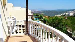 A balcony with a white balustrade overlooking a mountainous landscape with buildings in the distance.