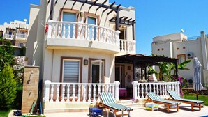 A two-story building with a balcony, a pool area with lounge chairs, and a covered patio.