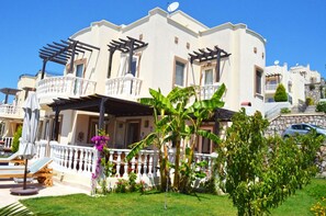 A multi-story building with balconies, a garden with tropical plants, and a pool area. - 3 Bedroom Apartment Lake View 10 by Likya Global (Milas)