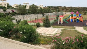 A playground with a climbing structure, slides, and a tennis court. - Apartment 3 Bedroom Lake View 8 by Likya Global (Milas)