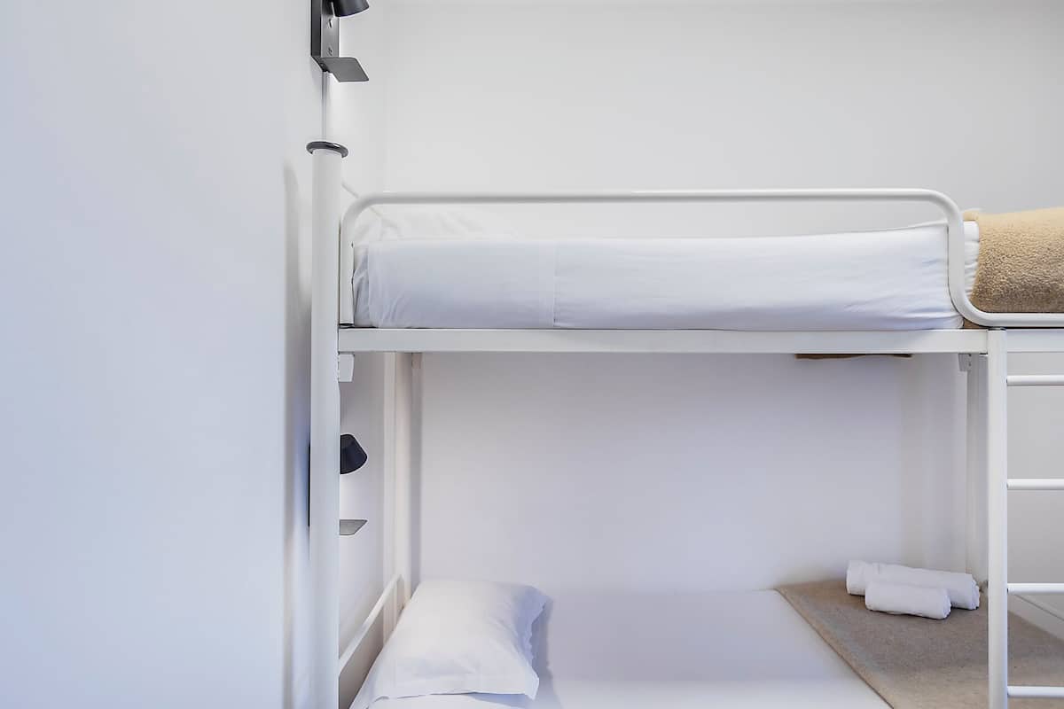 Un lit superposé avec un matelas blanc, un oreiller, une serviette et une petite étagère.