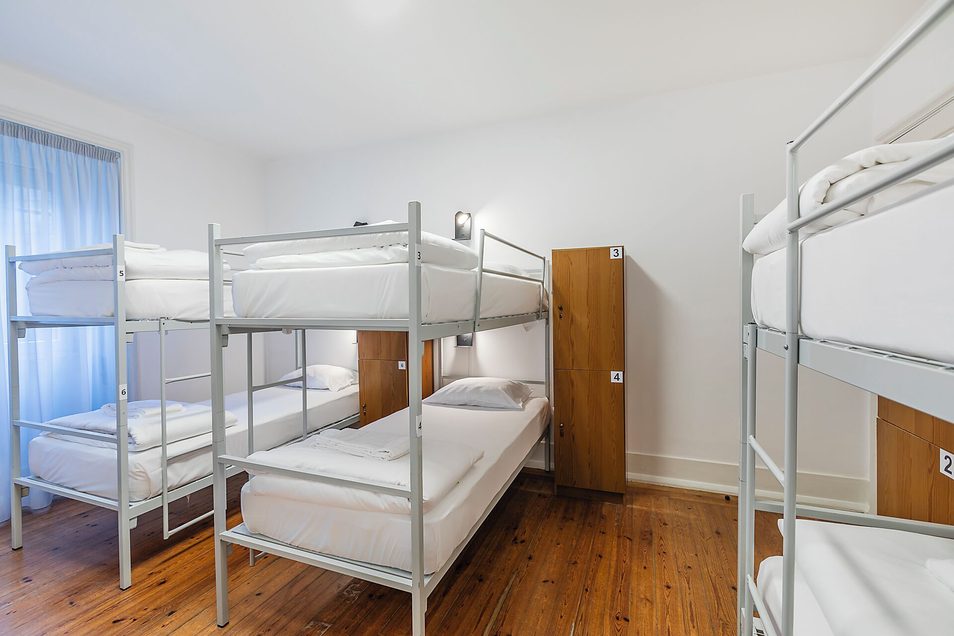 A bunk room with metal bunk beds, wooden wardrobe, and a window with curtains.