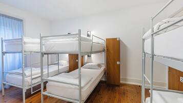 A bunk room with metal bunk beds, wooden wardrobe, and a window with curtains.
