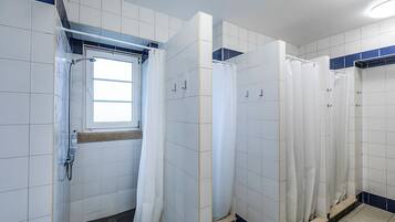 Uma casa de banho pública com azulejos brancos, uma janela e uma área de duche.