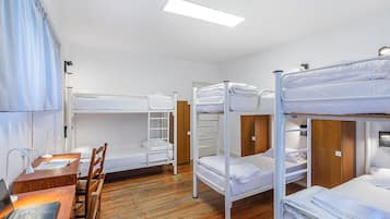Un dormitorio con literas, escritorios de madera y una computadora portátil.
