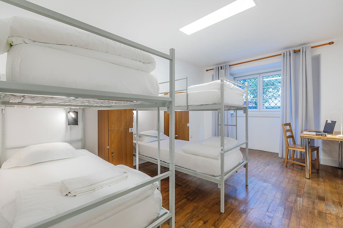 Une chambre avec un lit superposé, un bureau et une chaise, une fenêtre avec des rideaux et une porte.