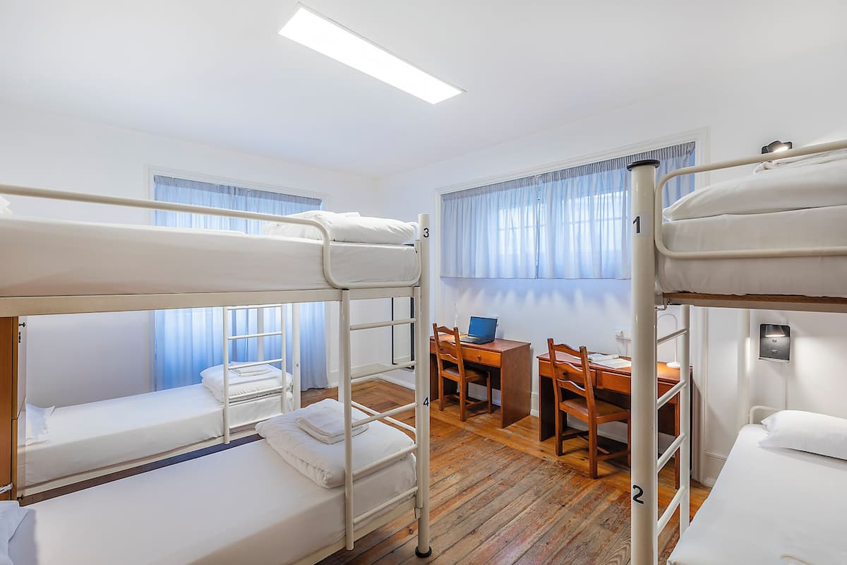 Une chambre avec trois lits superposés, un bureau avec un ordinateur portable et une chaise.
