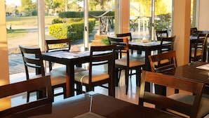 A restaurant with outdoor seating, large windows, and a view of a landscaped area.