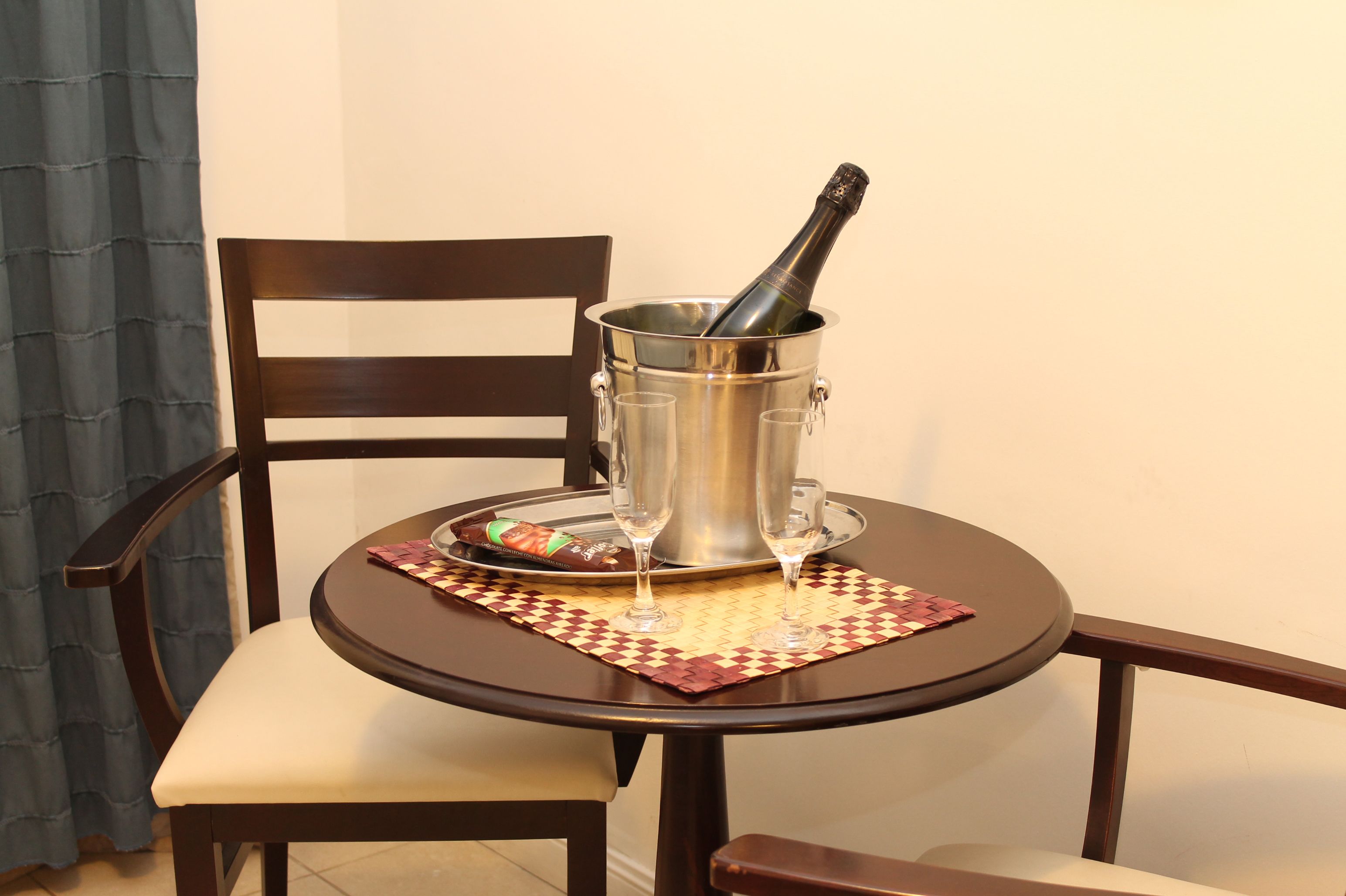 A dining table with a bottle of champagne, two glasses, and a plate of food.