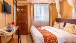 Una habitación de hotel con cama, escritorio, teléfono, televisor y ventana con cortinas.