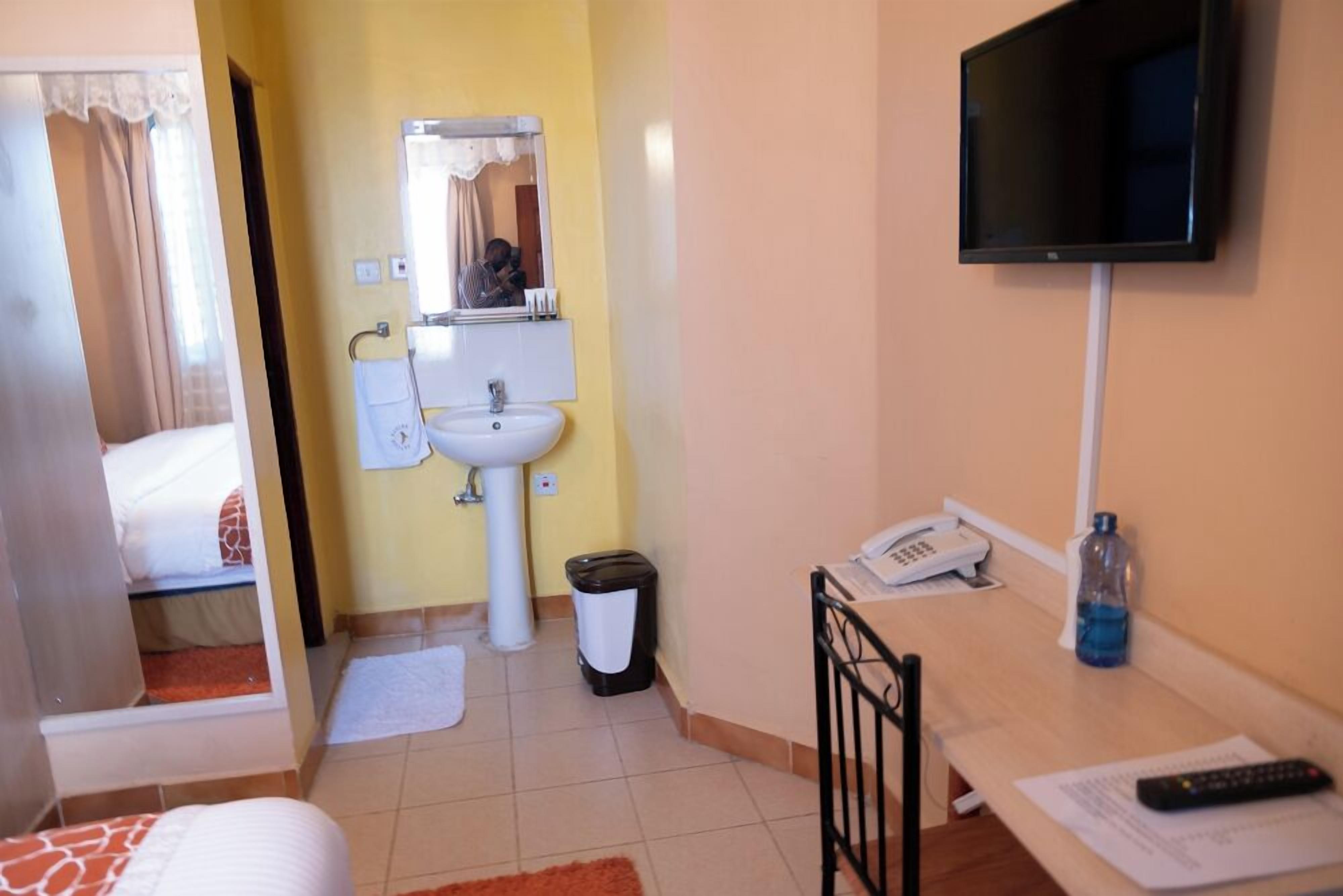 Une chambre d’hôtel équipée d’un lit, d’un lavabo, d’un miroir, d’une télévision, d’un bureau avec un téléphone et d’une poubelle.