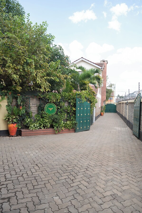 A paved pathway leading to a gated entrance with lush greenery and a sign reading "Casa de los Caballeros". - Javilla Eagles Safari Guest House (Nairobi)