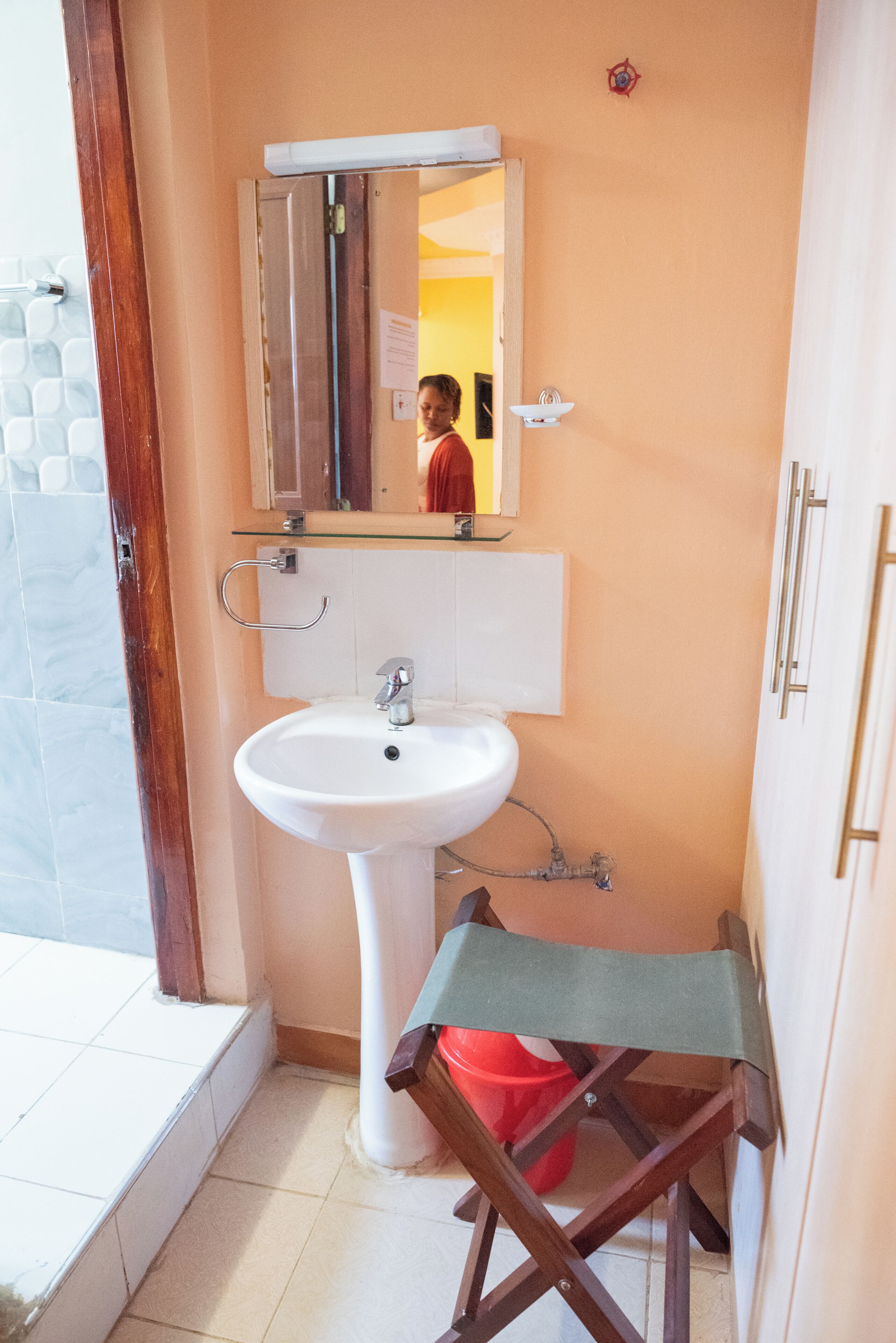 A bathroom with a white sink, a mirror above it, and a red bucket on the floor.