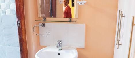 A bathroom with a white sink, a mirror above it, and a red bucket on the floor.