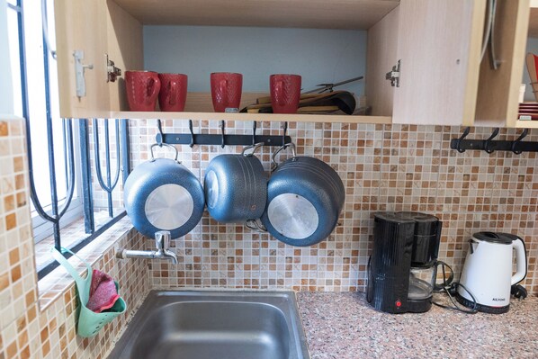 A kitchen with a sink, a coffee maker, and hanging pots. - Javilla Eagles Safari Guest House (Nairobi)