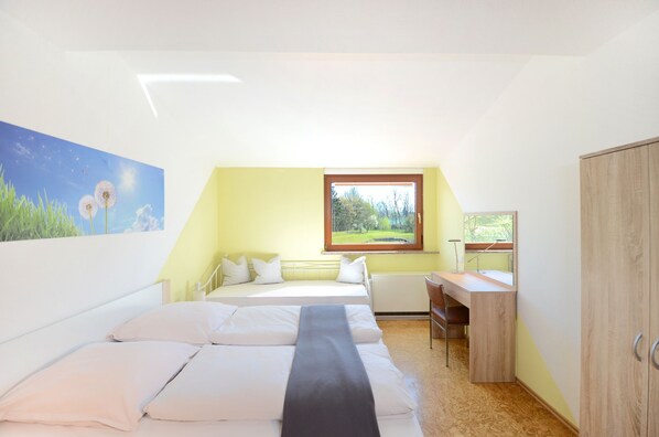 Una habitación con dos camas, un escritorio y una ventana con vistas a árboles.
