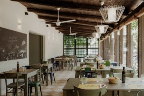 A restaurant with wooden ceiling beams, white pendant lights, and a checkered floor. Tables are set with chairs, glasses, and a menu. - Camping&Residence Il Pioppeto (Vasto)