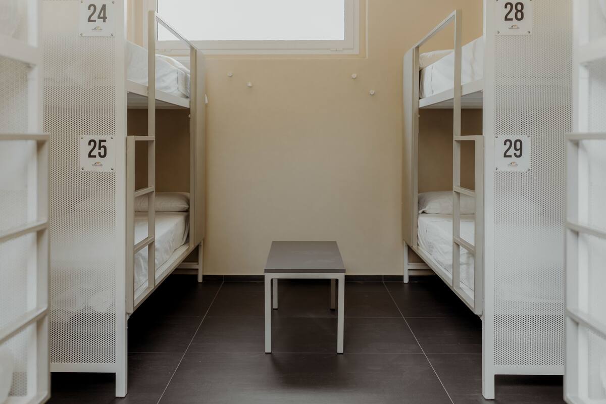 A dormitory room with bunk beds numbered 24, 25, 28, and 29, and a small table in the center.
