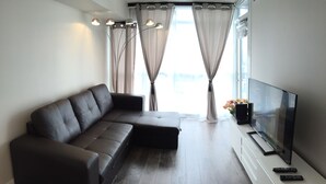 A modern living room with a sectional sofa, a flat-screen TV, and a remote control on a white console. - A&A Suites in the heart of Downtown Toronto (Toronto)