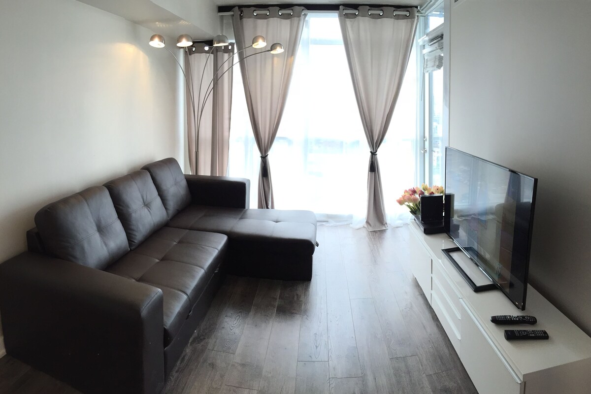 A modern living room with a sectional sofa, a flat-screen TV, and a remote control on a white console.