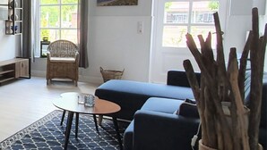 A living room with a blue sofa, a round coffee table, a wicker chair, and a rug. - Hotel Friesischer Hof (Hage)