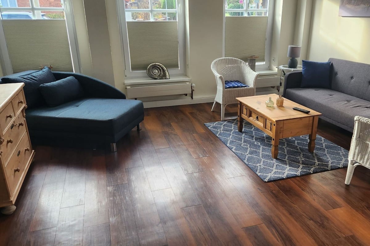 A living room with a dark blue sofa, a wooden coffee table, a grey sofa, a wicker chair, and a wooden dresser.