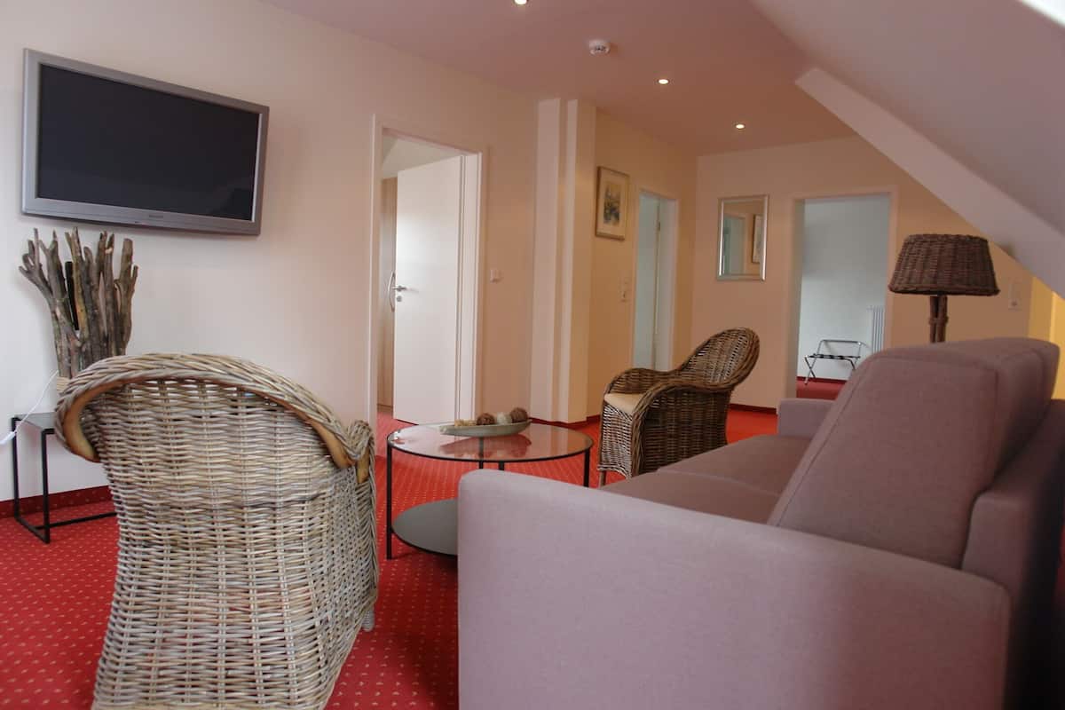 A living room with a sofa, wicker chairs, a small round table with a bowl, and a television on the wall.