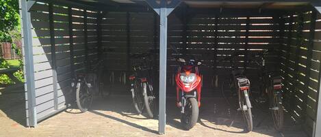 Un área de estacionamiento techada con varias bicicletas y una motocicleta roja.