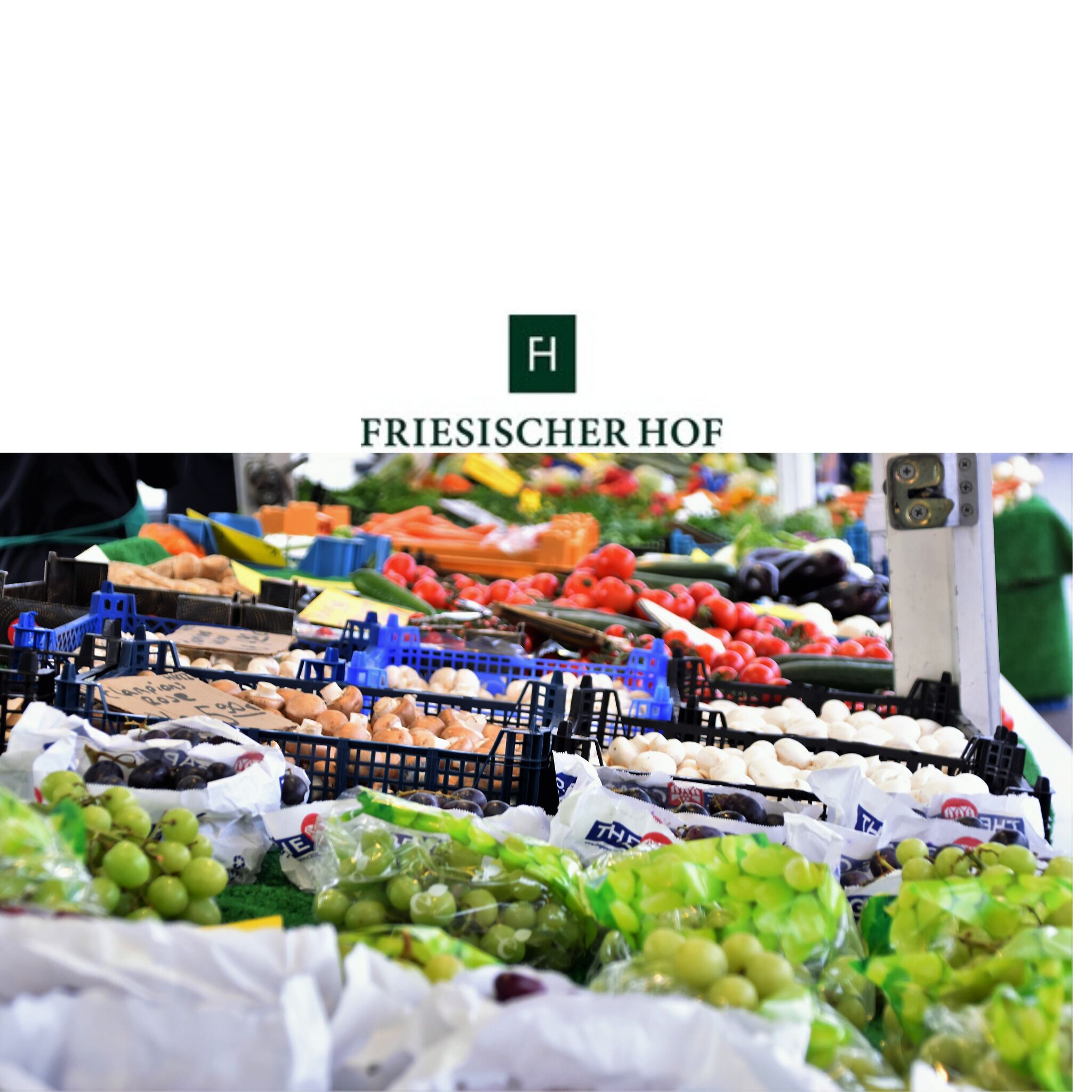 Un puesto de mercado con diversas frutas y verduras, como uvas, tomates y pepinos.