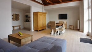 A spacious living area with a high ceiling, wooden beams, a dining set, and a television mounted on the wall. - Hotel Friesischer Hof (Hage)