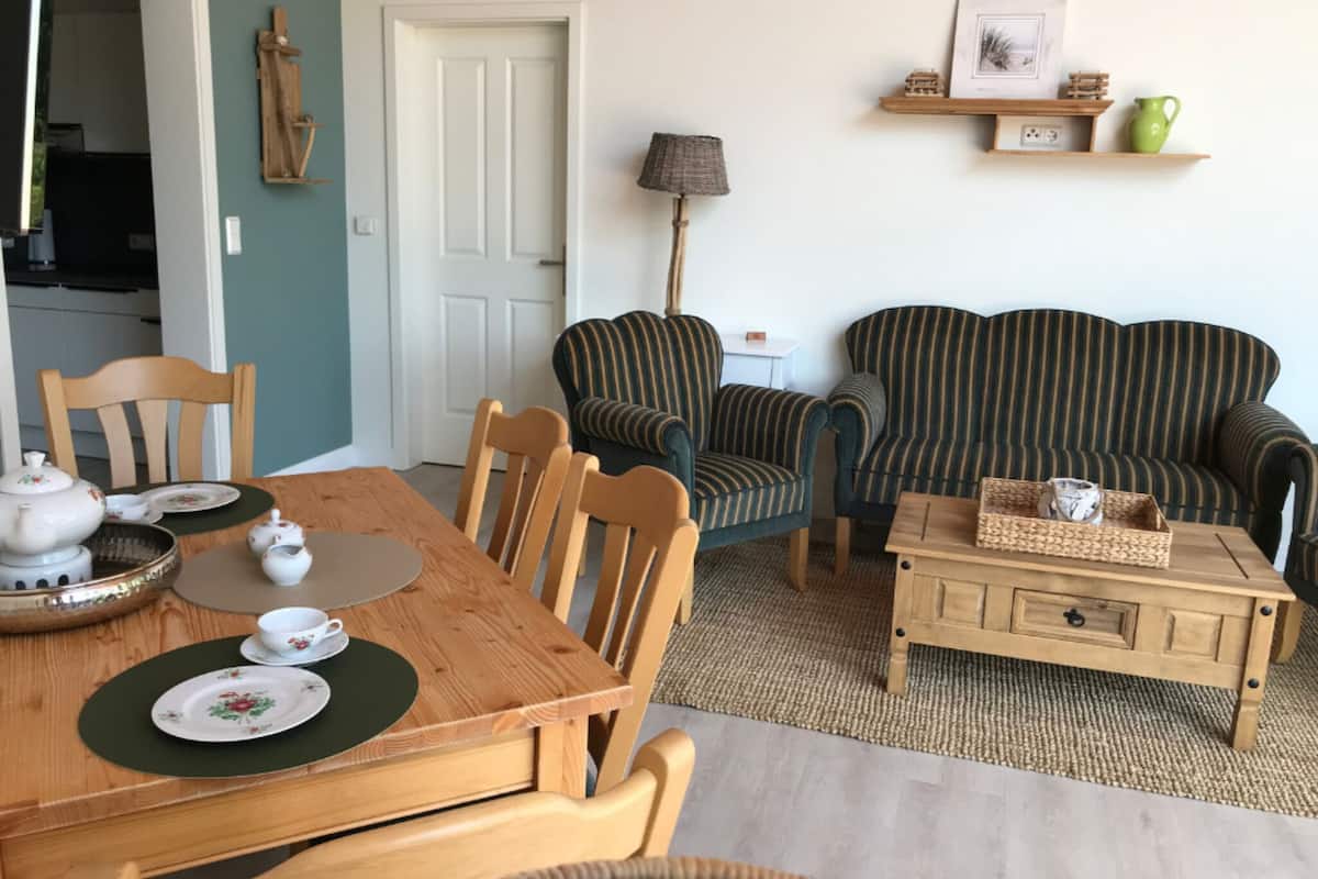 A dining area with a wooden table set for tea, two striped armchairs, a small wooden side table, and a lamp.