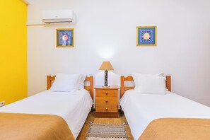 A double room with two beds, a bedside table with a lamp, an air conditioner, and two framed pictures on the wall. - HI Faro- Pousada de Juventude - Hostel (Faro)