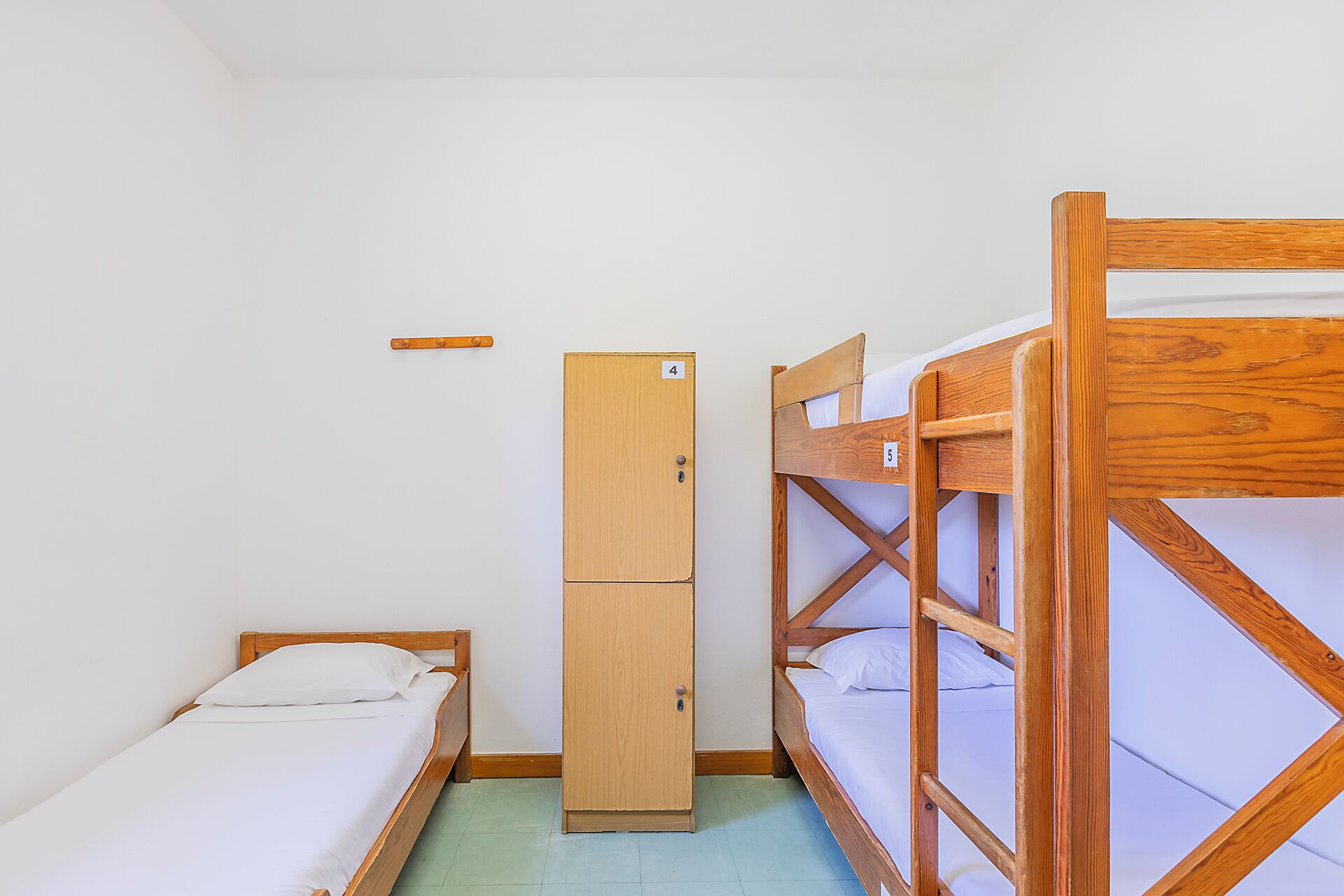 A dormitory room with bunk beds, a single bed, a wardrobe, and a small shelf.