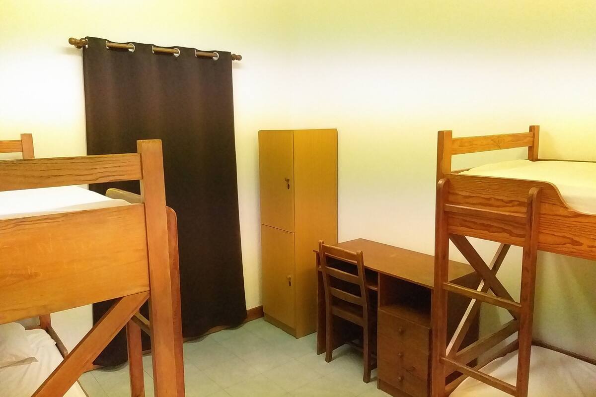Une chambre de dortoir équipée de deux lits superposés en bois, d’un bureau, d’une chaise et d’une armoire.