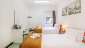 A hotel room with two beds, a desk, a chair, a lamp, a painting, and a window. - HI Faro- Pousada de Juventude - Hostel (Faro)