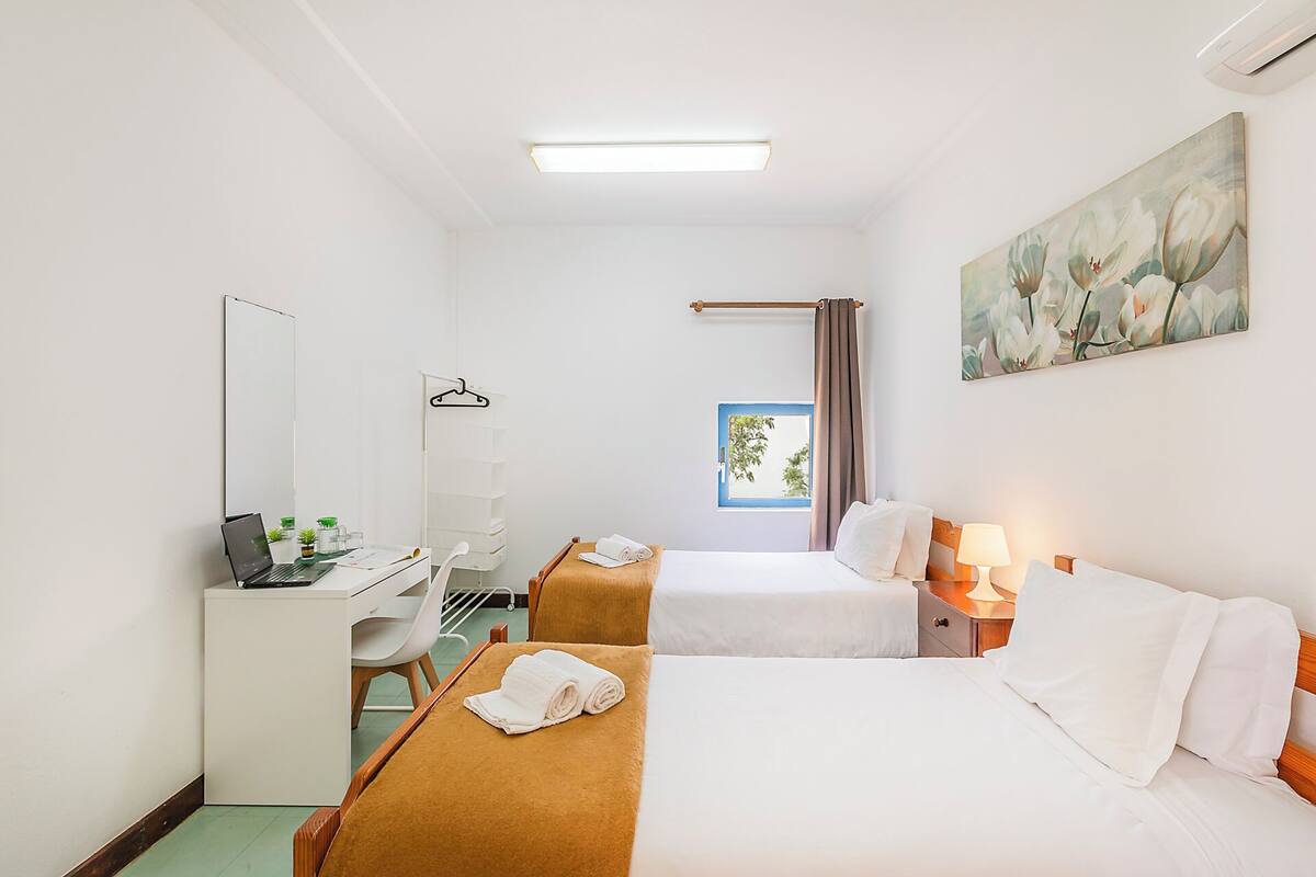 Une chambre d’hôtel avec deux lits, un bureau, une chaise, une lampe, un tableau et une fenêtre.